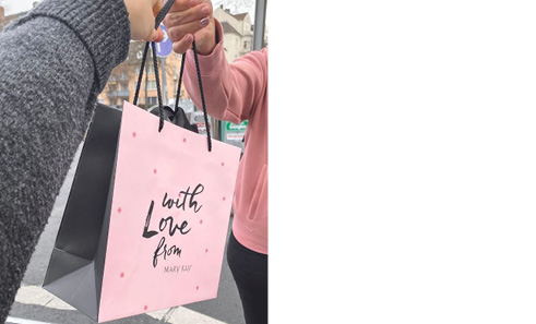 Een vrouw overhandigt een andere vrouw een tas met Mary Kay producten.