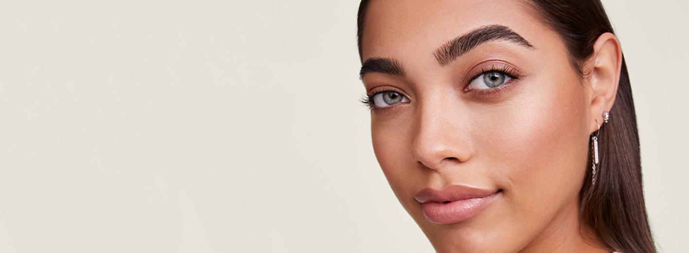 Een vrouw met een stralend frisse teint kijkt van opzij in de camera