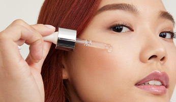 Een vrouw brengt met een pipet een paar druppels van de Mary Kay Clinical Solutions Ferulic + Niacinamide Brightener op haar wang aan – een booster die helpt het stralen van de huid te verbeteren