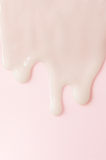 Voor een roze achtergrond zijn druppels van een huidverzorgingscrème te zien