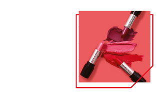 Drie Mary Kay Lipsticks in roze, paars en rood liggen op een roze achtergrond.