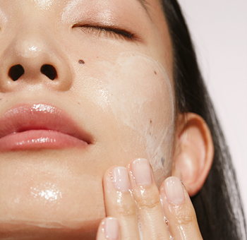 Een vrouw brengt Cleanser aan op haar gezicht met haar hand om haar gezicht te reinigen. Ze heeft haar ogen gesloten.