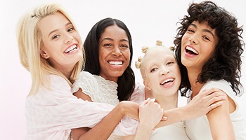 Vier vrolijke jonge vrouwen met verschillende huidskleuren en huidtypes omhelzen elkaar en glimlachen naar de camera