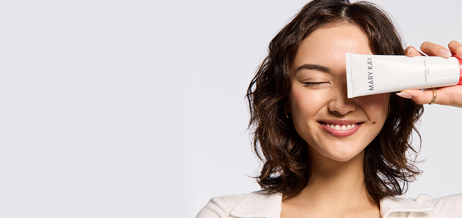 Een vrouw glimlacht, heeft één oog gesloten en houdt het nieuwe Mary Kay Hydrating Cream Mask voor haar andere oog.