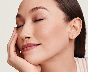 Een glimlachende jonge vrouw heeft haar ogen gesloten en ondersteunt haar gezicht in haar hand