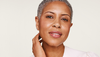 Een glimlachende vrouw met een stralende huid en grijs, kort haar pakt met één hand haar nek vast