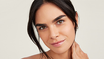 Een vrouw met kort bruin haar en een stralende huid lacht zijdelings naar de camera