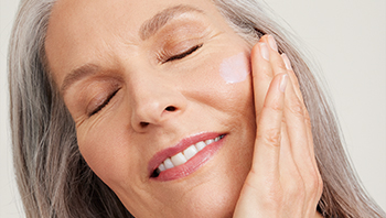 Een mooie, glimlachende vrouw die een Mary Kay Serum aanbrengt