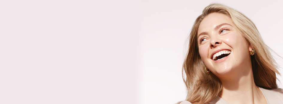 Een jonge vrouw (ongeveer 20 jaar) met een stralende huid lacht over haar schouder