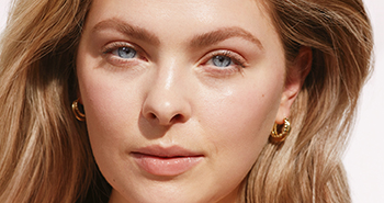 Een vrouw van begin 20 met een stralende, heldere huid lacht frontaal in de camera