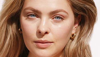 Een vrouw van begin 20 met een stralende, heldere huid lacht frontaal in de camera