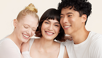 Twee vrouwen en één man van verschillende leeftijden met verschillende huidskleuren, huidskleuren en haarkleuren kijken in de camera. Ze hebben allemaal een stralende, heldere huid.