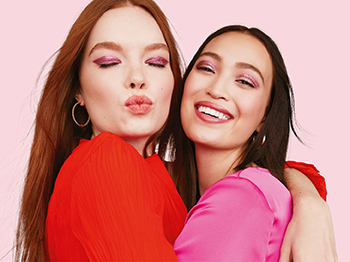 Twee vrouwen met opvallend opgemaakte lippen en ogen en opzichtige topjes omhelzen elkaar