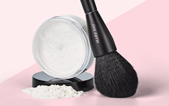 Een open potje Mary Kay Translucent Loose Powder met overlopend poeder naast een All-Over Powder Brush voor een tweekleurige roze achtergrond