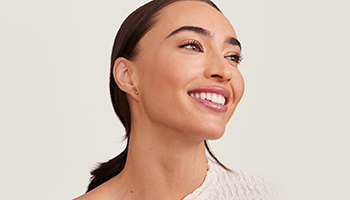 Een vrouw met markante wenkbrauwen en steil bruin haar achter de schouders, die met gesloten ogen lacht en haar neus enigszins rimpelt