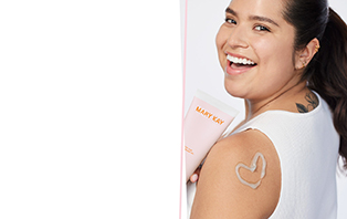 Een vrouw is van achteren te zien. Ze glimlacht over haar schouder, houdt een tube Mary Kay After Sun Body Lotion in haar hand en op haar schouder is met witte lotion een hart getekend.