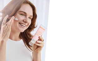 Een vrouw brengt met één hand Mary Kay Mineral Facial Sunscreen met beschermingsfactor 30 aan op haar gezicht. In haar andere hand houdt ze de tube met gezichtszonnebrandcrème vast.