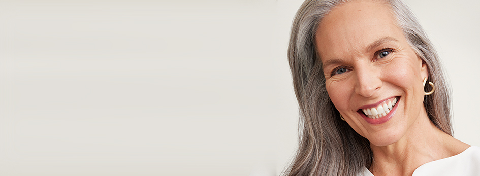 Een vrouw van boven de 60 met een rijpe, verzorgde huid en een kort kapsel lacht zijdelings naar de camera