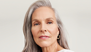 Een vrouw van boven de 60 met een rijpe, verzorgde huid en een kort kapsel lacht zijdelings naar de camera