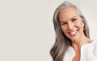 Een vrouw van boven de 60 met een rijpe, verzorgde huid en een kort kapsel lacht zijdelings naar de camera