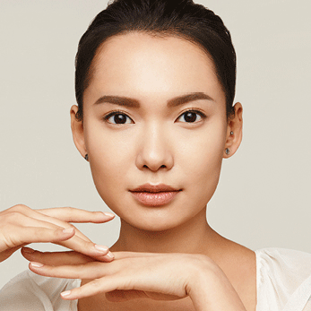 Een brunette vrouw kijkt frontaal in de camera. Afzonderlijke delen van haar gezicht worden met verschillende kleuren belicht - met behulp van face mapping worden deze delen van het gezicht met verschillende maskers behandeld = multimasking.