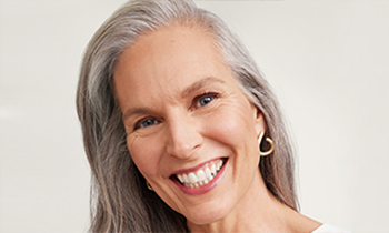 Een vrouw van boven de 60 met een rijpe, verzorgde huid en een kort kapsel lacht zijdelings naar de camera