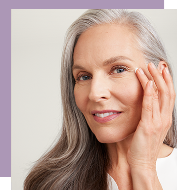 Een vrouw met een rijpe huid glimlacht naar de camera en raakt met haar hand haar wang aan