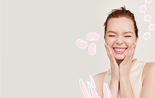 Een glimlachende vrouw met een stralende teint heeft haar ogen gesloten en raakt met beide handen haar gezicht aan. Moleculen en ingrediënten zijn om haar heen getekend.