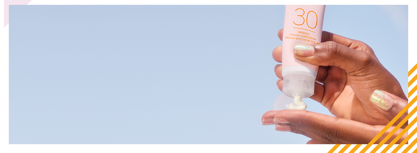 Een hand met een donkere huidskleur voor een stralend blauwe achtergrond drukt voorzichtig wat zonverzorging in de andere hand.