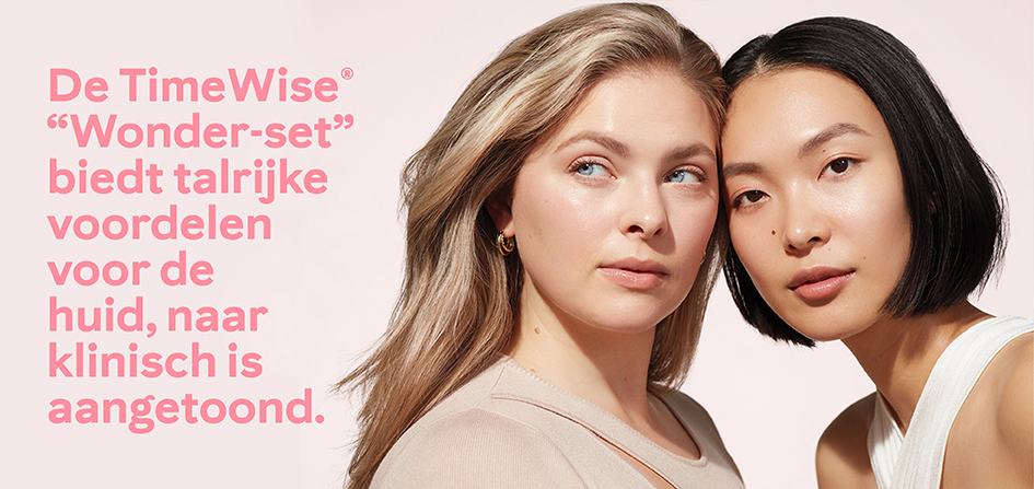 Een blonde en een brunette Aziatische vrouw poseren zelfverzekerd dicht bij elkaar omringd door zonlicht en een lichtroze achtergrond