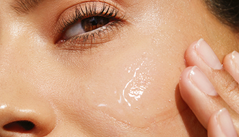 Close-up van een brunette vrouw die zelfverzekerd naar de camera kijkt terwijl ze gezichtsverzorging op haar wang aanbrengt