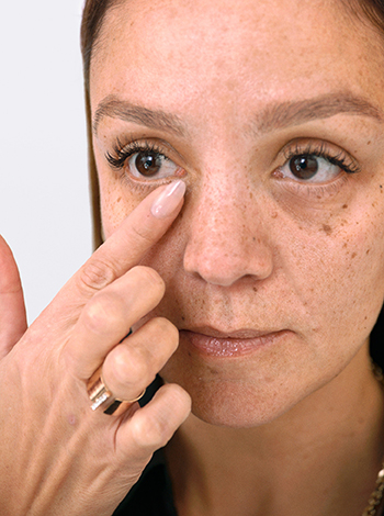 Een vrouw brengt met één vinger concealer aan onder haar oog.