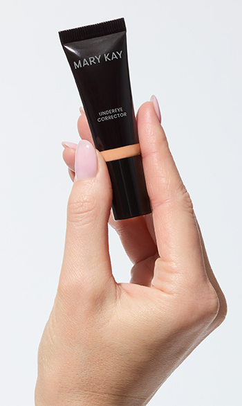 Close-up van een hand die een tube Undereye Corrector van Mary Kay in een lichte kleur vasthoudt.