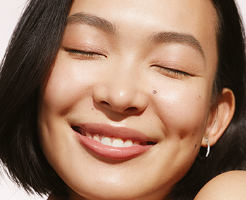 Macro-opname van een Aziatische vrouw die met gesloten ogen glimlacht, omgeven door zonlicht