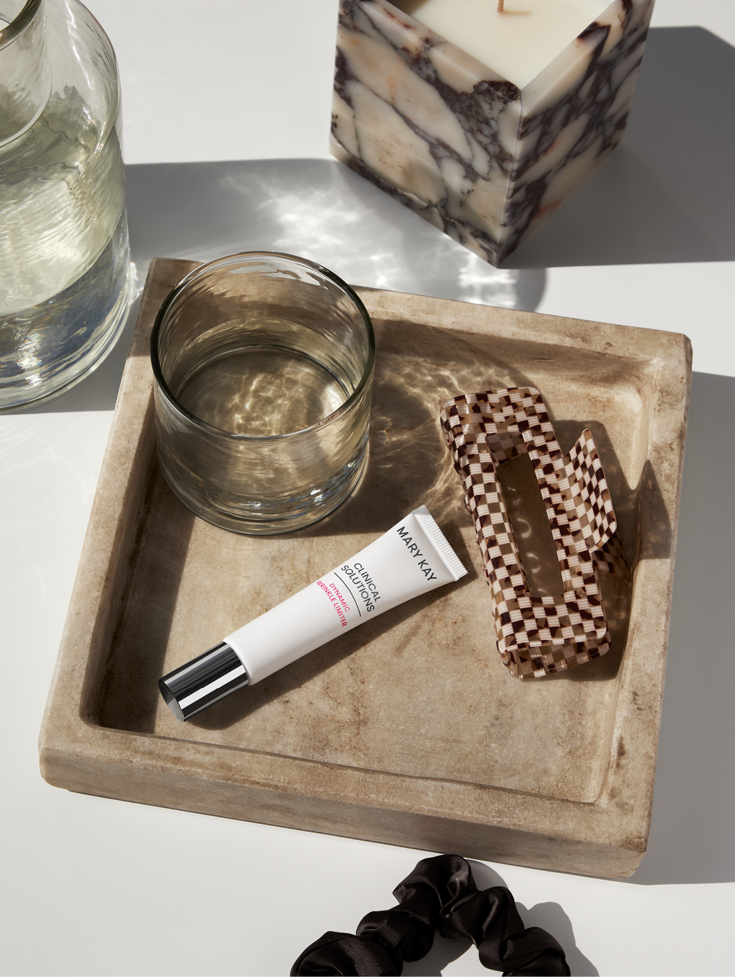 Een klein bakje bevat een haarspeld, een glas water en de Clinical Solutions Dynamic Wrinkle Limiter van Mary Kay