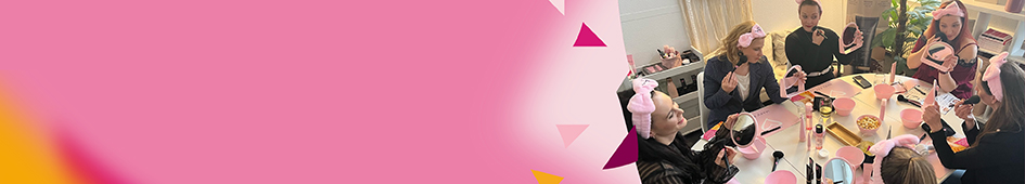 Enkele vrouwen met roze haarbanden zitten aan een tafel om gezichtsverzorgingsproducten en make-up uit te proberen op een Mary Kay party, samen met een zelfstandige schoonheids consulente met Mary Kay.